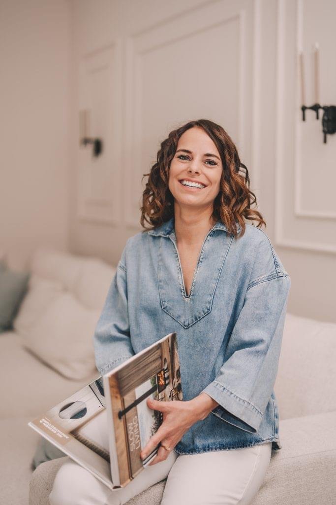 Viktoria Semmler sitzt mit einem Slow Living Interior Design Buch auf dem Sofa und lächelt in die Kamera